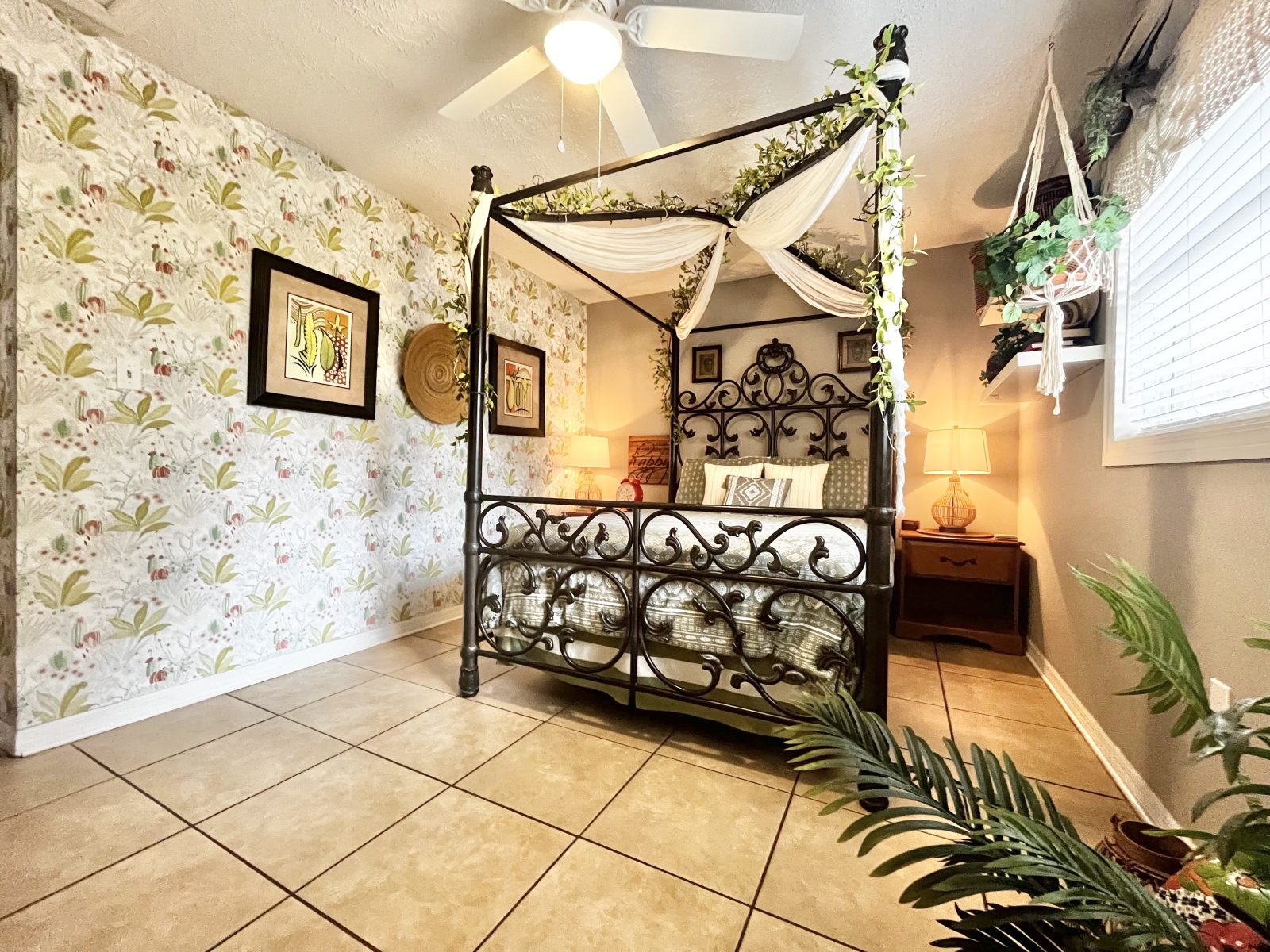 Tropical bedroom with iron canopy bed, botanical wallpaper and plants