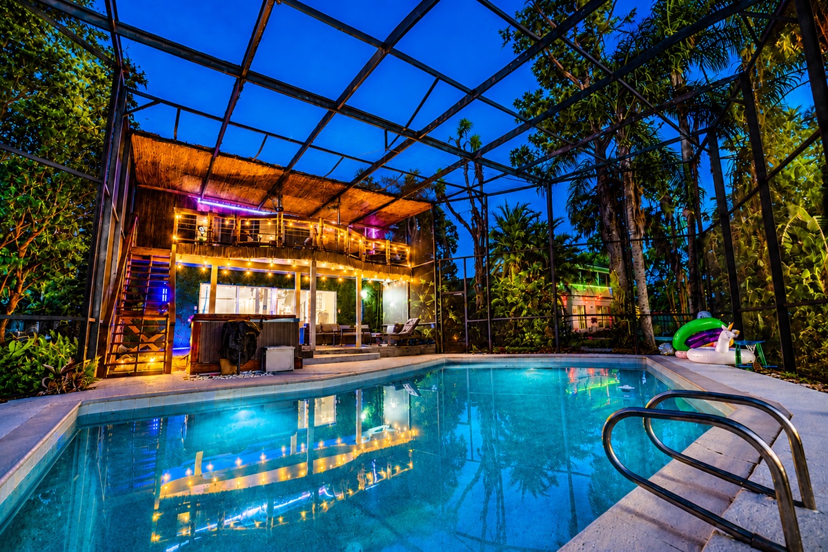 Screened pool at dusk facing the tiki loft bar with string lights