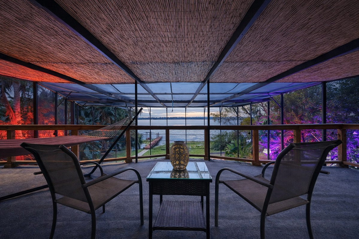 Tiki balcony at dusk with hammock, colorful uplighting and lake view
