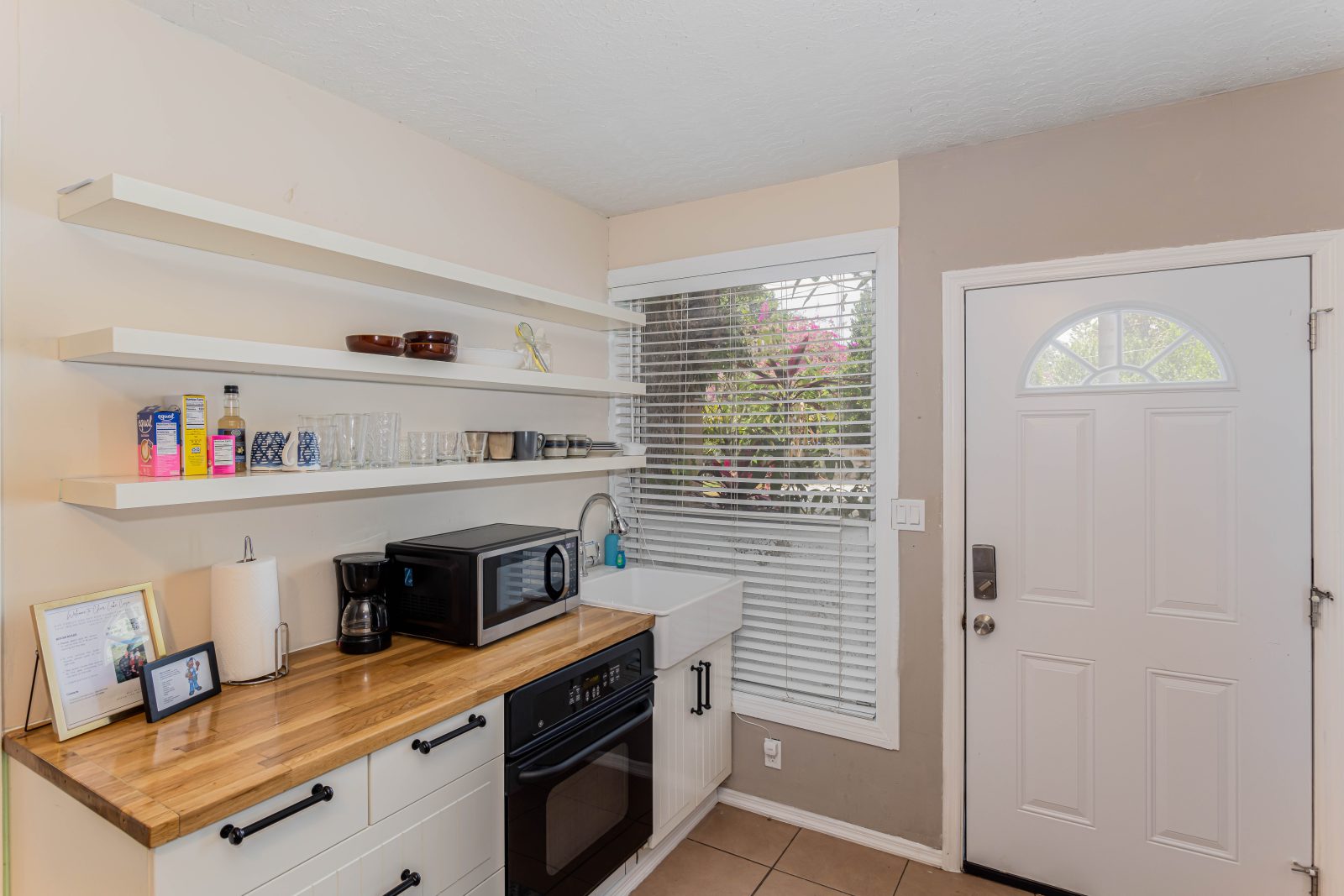 Kitchenette with butcher-block counter, open shelves, oven and farmhouse sink