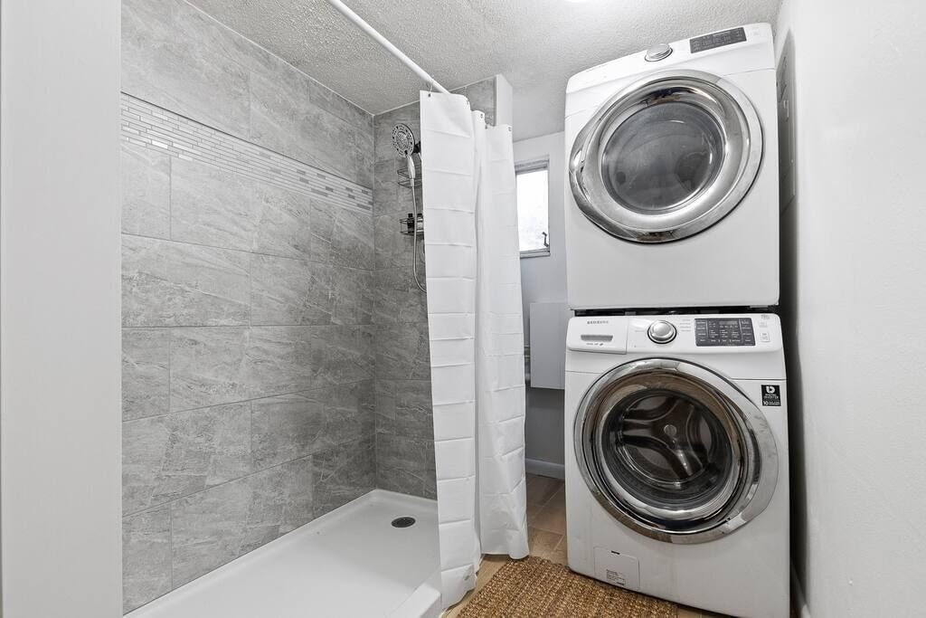 Laundry area with stacked washer and dryer beside a tiled shower